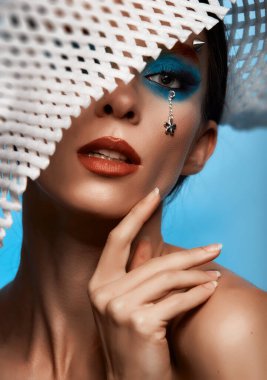 Moda yaratıcı makyaj. Temiz ve parlak ciltli genç bir kadının güzel portresi ve parlak mavi bir arka planda duran yapay elmaslarla süslenmiş.