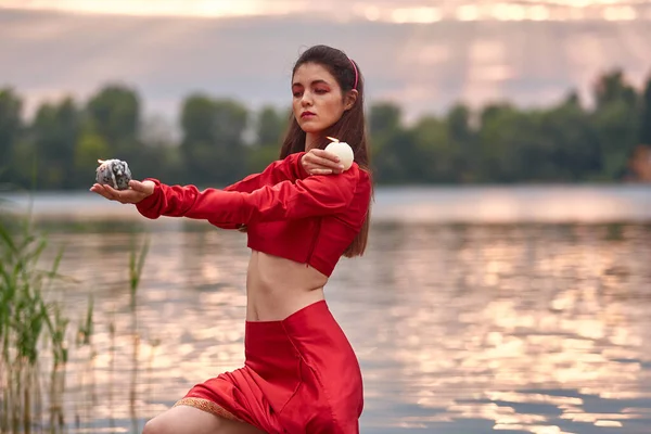 Ritual dance with candles in hands. Brunette woman in red costume for belly-dance is dancing on the beach