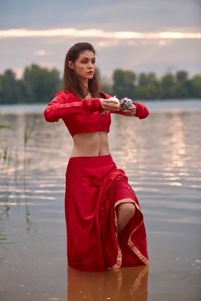 Ritual dance with candles in hands. Brunette woman in red costume for belly-dance is dancing on the beach