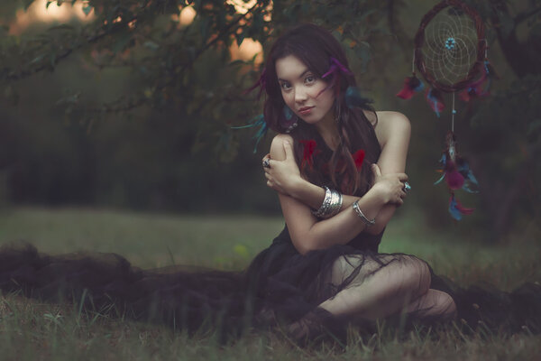 Portrait of a beautiful woman with feather in her hair. Boho fashion style. Sitting on the gras