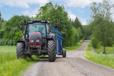 Traktör ve karavan, yazın tarlada yol kenarında duruyor. Ormana yakın bulutlar altında, gökyüzünün altında hasat sırasında..