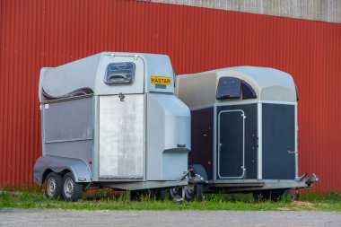 Kırmızı İskandinav hangarının yakınındaki çimlerin üzerine park edilmiş modern at nakliye karavanları..