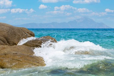 Ege Denizi Mavi Dalgaları, Chalkidiki Kayalıkları 'na çarpıyor. Arka planda Athos Dağı var. Güneşli bir günde, deniz ve gökyüzü bulutlu.