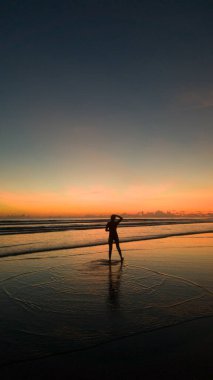 Genç bir kadın güzel bir gün batımında sahilde duruyor.