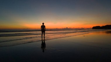Genç adam güzel bir gün batımında sahilde duruyor.