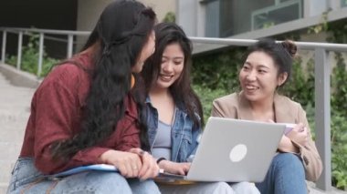 Bir grup Asyalı kız öğrenci dizüstü bilgisayar kullanıyor ve merdivenlerde birlikte çalışıyorlar.