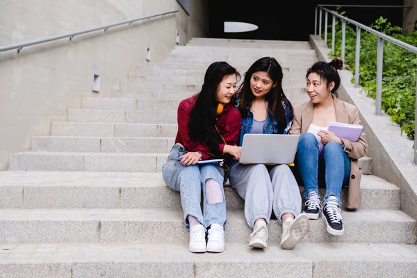 Ázsiai diákokból álló csoport, akik laptopot használnak és együtt tanulnak, miközben az egyetemi campus lépcsőjén ülnek. — Stock Fotó