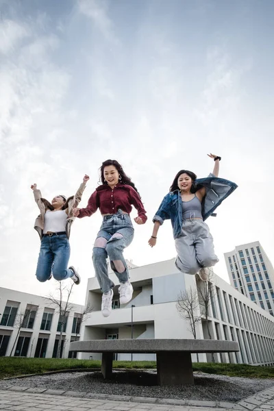 Porträt einer Gruppe asiatischer Freundinnen, die die gemeinsame Zeit genießen, während sie im Freien in der Luft springen. — Stockfoto