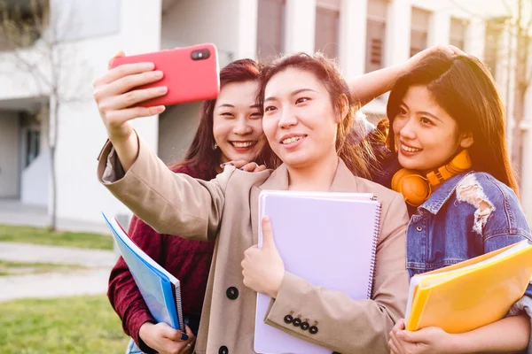 Asyalı üniversite öğrencileri üniversite kampüsünün dışında dururken cep telefonlarıyla selfie çekiyorlar. Eğitim kavramı. — Stok fotoğraf