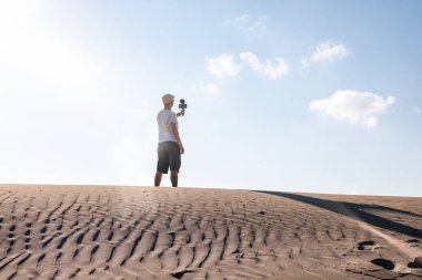 Adam kendini cep telefonuyla çöl kumullarında filme çekiyor. Gezgin erkek içerik oluşturucu