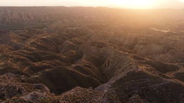 Uçan insansız hava aracı engin ve engebeli bir çöl kanyonu üzerinde uçuyordu. Altın gün batımı ışığı, kurumuş, aşınmış tepeleri ve oluşumları aydınlatır. Gorafe, Granada, İspanya