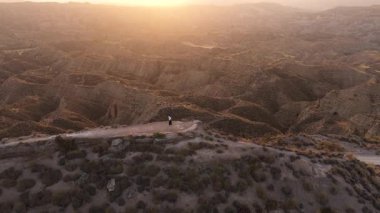 Uçurumun kenarında duran yalnız bir kadının uçsuz bucaksız, çorak bir kanyon manzarasına bakan güneş uzaklardan batarken görüntüsü.