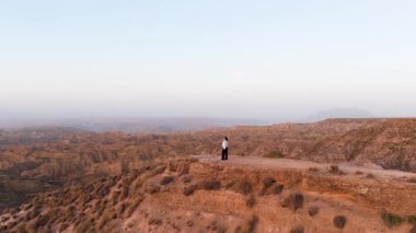 Uçurumun kenarında tesettür takmış bir kadının güzel bir günbatımında uçsuz bucaksız ve çorak bir çöl kanyonuna bakışının havadan görüntüsü.