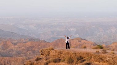 Kolları başarı ve özgürlük içinde bir dağın tepesinde yükselen Müslüman bir kadın. Arka planda geniş ve destansı çöl manzarası