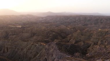 Geniş hava manzarası kanyonlar ve aşınmış dağlarla birlikte geniş ve kurak bir arazide yavaşça hareket ediyor. Batan güneşin sıcak ışığı sahneyi yıkıyor. Gorafe, Granada, İspanya