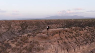 Uçurumun kenarından gün batımında uçsuz bucaksız bir çöl kanyonunda nefes kesici manzaraya hayran olan genç bir çiftin çarpıcı hava perspektifi.