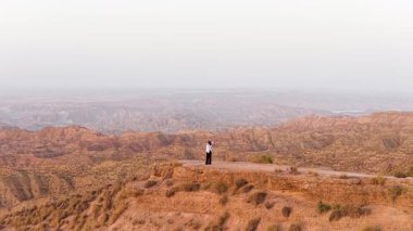 Uçurumun kenarında duran, kollarını kaldıran bir kadının uçsuz bucaksız bir çöl kanyonu manzarasına bakarken görüntüsü.