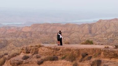 Uçurumun kenarında kucaklaşan sevgi dolu bir çiftin havadan görünüşü. Erkek ve kadın, manzaralı çöl manzarasının tadını çıkarırken samimi bir anı paylaşıyorlar.
