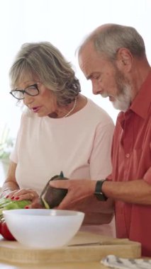 Yaşlı bir çift birlikte avokado soyuyorlar, takım çalışması sergiliyorlar ve mutfakta sağlıklı beslenme alışkanlıkları var. Dikey görüntüler