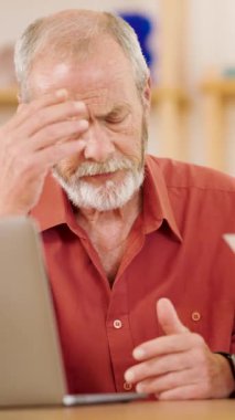 Yaşlı bir adam dizüstü bilgisayarındaki kötü haberlere tepki göstererek endişe, endişe ve stresi dile getiriyor. Dikey görüntüler