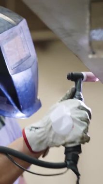 Koruyucu teçhizat kullanan endüstriyel işçiler metal bir dikişe kaynak yapmak için tig meşalesi kullanıyorlar. Üretim sürecine parlak kıvılcımlarla yakından bakın. Dikey görüntüler