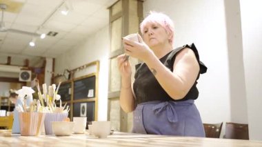 Profesyonel seramikçi, el yapımı seramik kaseyi dikkatle incelerken sanatsal çömlek atölyesinde çalışırken, sanatçılık ve yaratıcı tasarım sürecini gözler önüne seriyor.