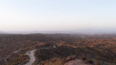 Uçurumun kenarında duran yalnız bir kadın gün batımında engin ve kurak bir kanyon manzarasına bakıyor. Havadan çekilen çekim geniş çöl arazisini ortaya çıkarıyor.