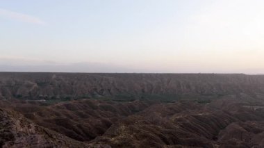 Günbatımında engebeli kanyonlar, çorak tepeler ve derin vadilerle dramatik bir çöl manzarasının üzerinde yavaşça uçan geniş bir hava manzarası. Gorafe, Granada, İspanya