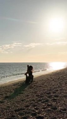 Aktif kıyafetli yetişkin bir kadın, gün doğumunda okyanus kıyısındaki kumlu sahilde huzurlu bir enerjiyle uzanıyor.