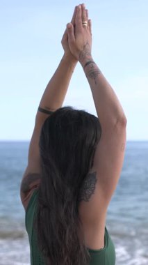 Yeşil spor kıyafetli yetişkin kadın güneşin doğuşunda sakin odak ve sakin okyanus zeminiyle Urdhva Hastasana yogası yapıyor.