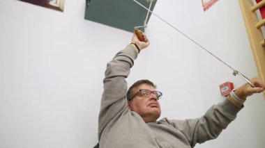 Tekerlekli sandalyedeki kararlı adam kollar ve omuzlar için fizyoterapi egzersizleri yapıyor, iyileşmek için makara makinesine ip çekiyor.