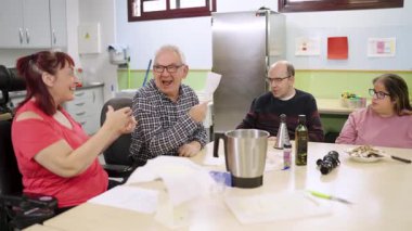 Engelli bir grup insan yemek atölyesi sırasında bir masada gülüp sohbet ediyorlar. Toplumsal katılım ve bütünleşme kavramı