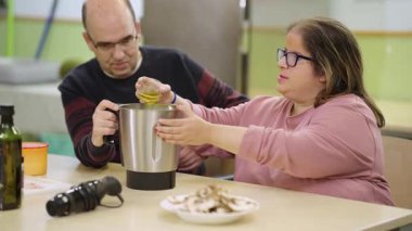 Bozuk sendromlu bir kadına zeytinyağı döken yardımcı bir bakıcı. Engelliler için bir yemek sınıfındalar.