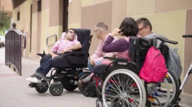 Engelli bir grup arkadaş bir şehir caddesinde konuşuyorlar ve eğleniyorlar. Bir adam elektrikli sandalyede.