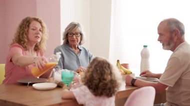 Nesiller boyu sağlıklı bir kahvaltı yapan mutlu bir aile. Bir anne kızı için portakal suyu dökerken büyükannesi ve büyükbabası izleyip sohbet eder.