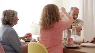 Bir grup mutlu kıdemli arkadaş evde sağlıklı bir kahvaltı yapıyorlar. Sevimli yaşlı adam ve kadınlar masada konuşuyor ve gülüyorlar.
