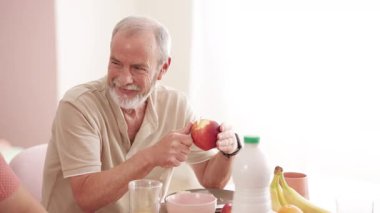 Kahvaltı masasında bıçakla kırmızı bir elmayı soyarken gülümseyen mutlu kıdemli adam. Yaşlılar için sağlıklı yaşam tarzı ve beslenme