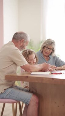 Şefkatli büyükanne ve büyükbabalar, küçük torunlarıyla güzel vakit geçiriyorlar. Tahta bir masada birlikte otururken ona resim çizmeyi ve resim yapmayı öğretiyorlar. Dikey görüntüler