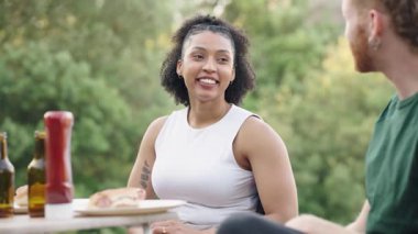 Parkta yemek ve içeceklerle piknik yaparken gülümseyen, gülen ve sohbet eden mutlu genç bir çift.