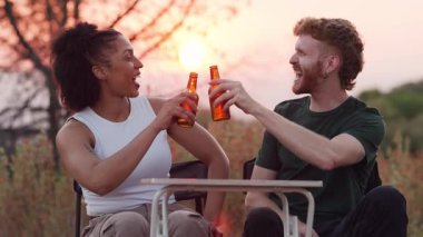 Romantik bir buluşmadan zevk alan genç bir çift, bira şişeleriyle kadeh kaldırıyor ve güzel bir altın saat boyunca dışarıda birlikte gülüyorlar.