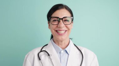 Mutlu bir kadın doktorun portresi gülümseyen ve kameraya poz veren. Laboratuvar önlüğü ve steteskop giyen profesyonel bir tıp çalışanı.