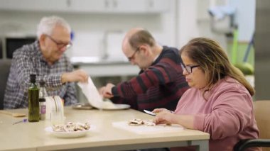 Engelli bir grup insan yemek kursuna katılıyor. Tekerlekli sandalyede bir kadın kesim tahtasıyla mantar kesiyor.