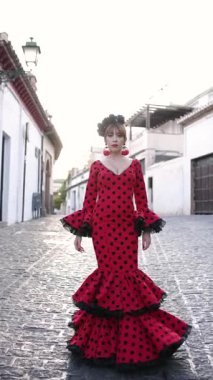 Kültürel bir olay sırasında İspanyol köyünün klasik dar bir sokağında geleneksel kırmızı benekli elbisesiyle flamenko dansı yapan güzel bir kadın.