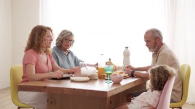 Üç nesildir yemek masasında oturup yemek yiyen ve konuşan mutlu bir aile. Büyükanne ve büyükbabalar, kızları ve torunlarıyla yemek yiyorlar.