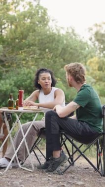 Çok ırklı, genç bir çift romantik bir pikniğin tadını çıkarıyor, sakin, doğal bir parkta katlanan bir masada oturup yemek yiyor ve sohbet ediyorlar.