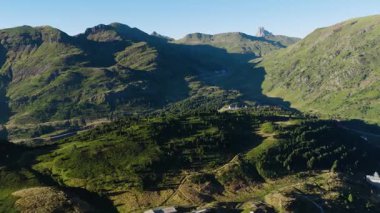 Derin vadileri ve berrak mavi gökyüzünün altında göze çarpan tepeleri olan yemyeşil bir sıradağ boyunca hareket eden nefes kesici hava görüntüleri.