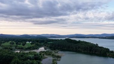 Sersemletici hava manzarası sakin bir akşamda yemyeşil ormanlar ve tepelerle çevrili engin bir göl dramatik bulutlu bir gökyüzü altında