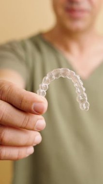 Şeffaf bir ortodontik hizalayıcı tutan gülümseyen bir adamın yakın çekimi. Diş bakımı ve güzel bir gülümseme. Dikey