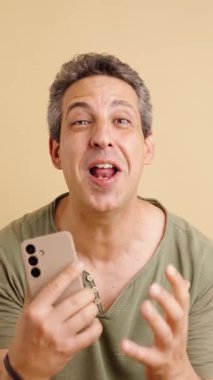 Beyaz saçlı mutlu beyaz adam akıllı telefonuna bakarken kutlama yapıyor. Kollarını zaferle kaldırarak büyük bir sürpriz ve sevinç gösteriyor. Dikey