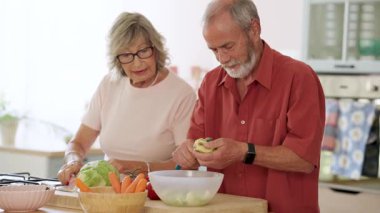 Olgun bir çift birlikte mutfaklarında çalışıyor, dikkatli bir şekilde taze elmaları soyarken aynı zamanda neşeli yemek hazırlama ve sağlıklı beslenme anlarını paylaşıyorlar.